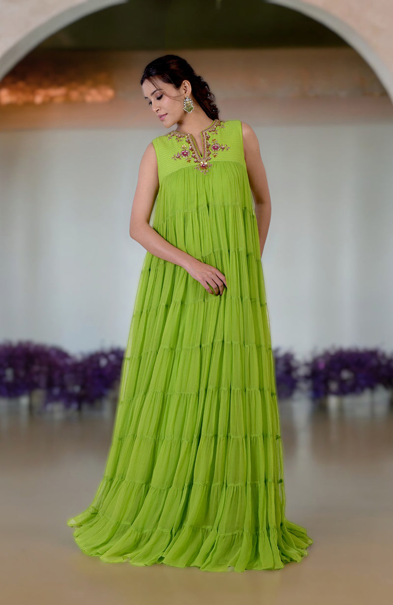 A woman models a vibrant green tiered dress with intricate zardozi embroidery on the neckline.