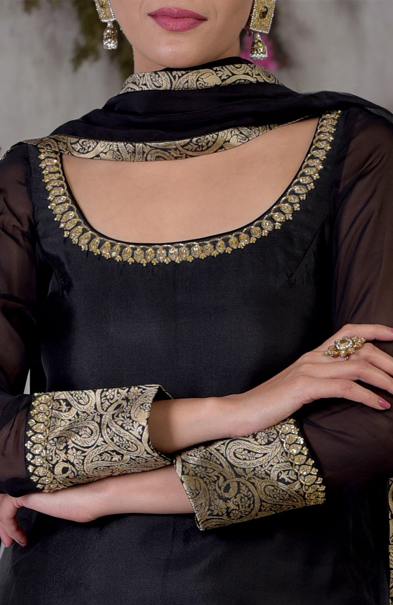 A woman models a black and gold Banarasi embroidered sharara set with a matching dupatta.