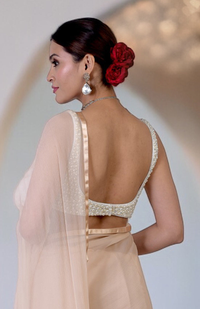 A woman models a white pearl hand-beaded blouse with an open back and a peach saree.