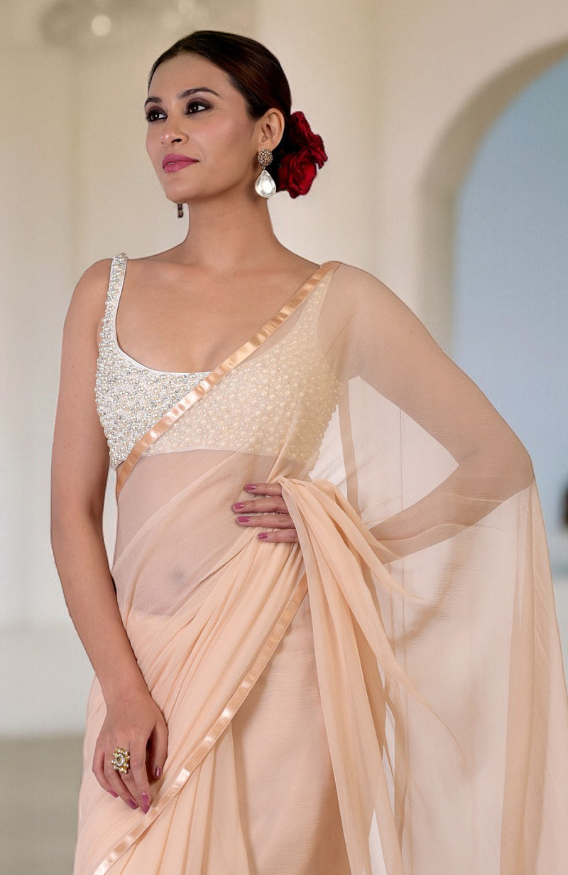 A woman models a white pearl hand-beaded blouse with a peach saree.