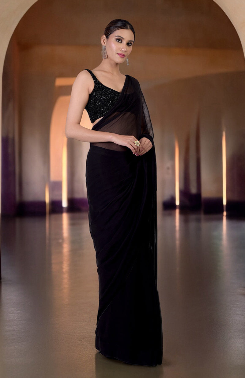 A woman models a black hand-beaded blouse with a matching chiffon saree.