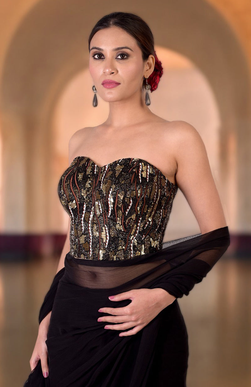 A woman models a black hand-embroidered corset with gold and black embellishments.