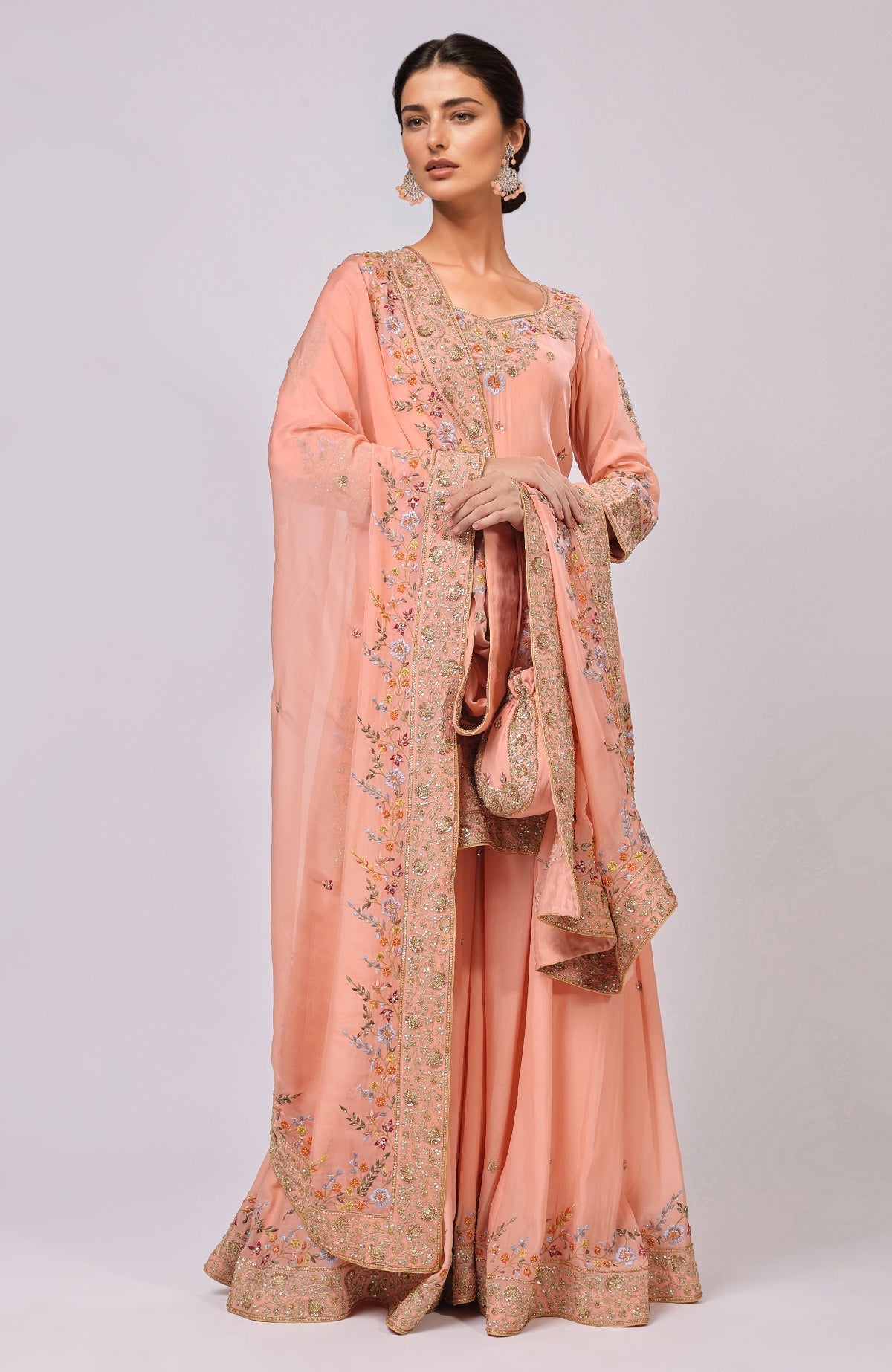 A model wears a salmon marori and resham hand-embroidered sharara set with a matching potli bag.