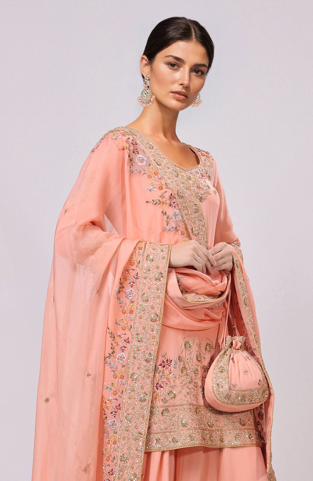 A woman models a salmon sharara set with intricate gold and floral embroidery.