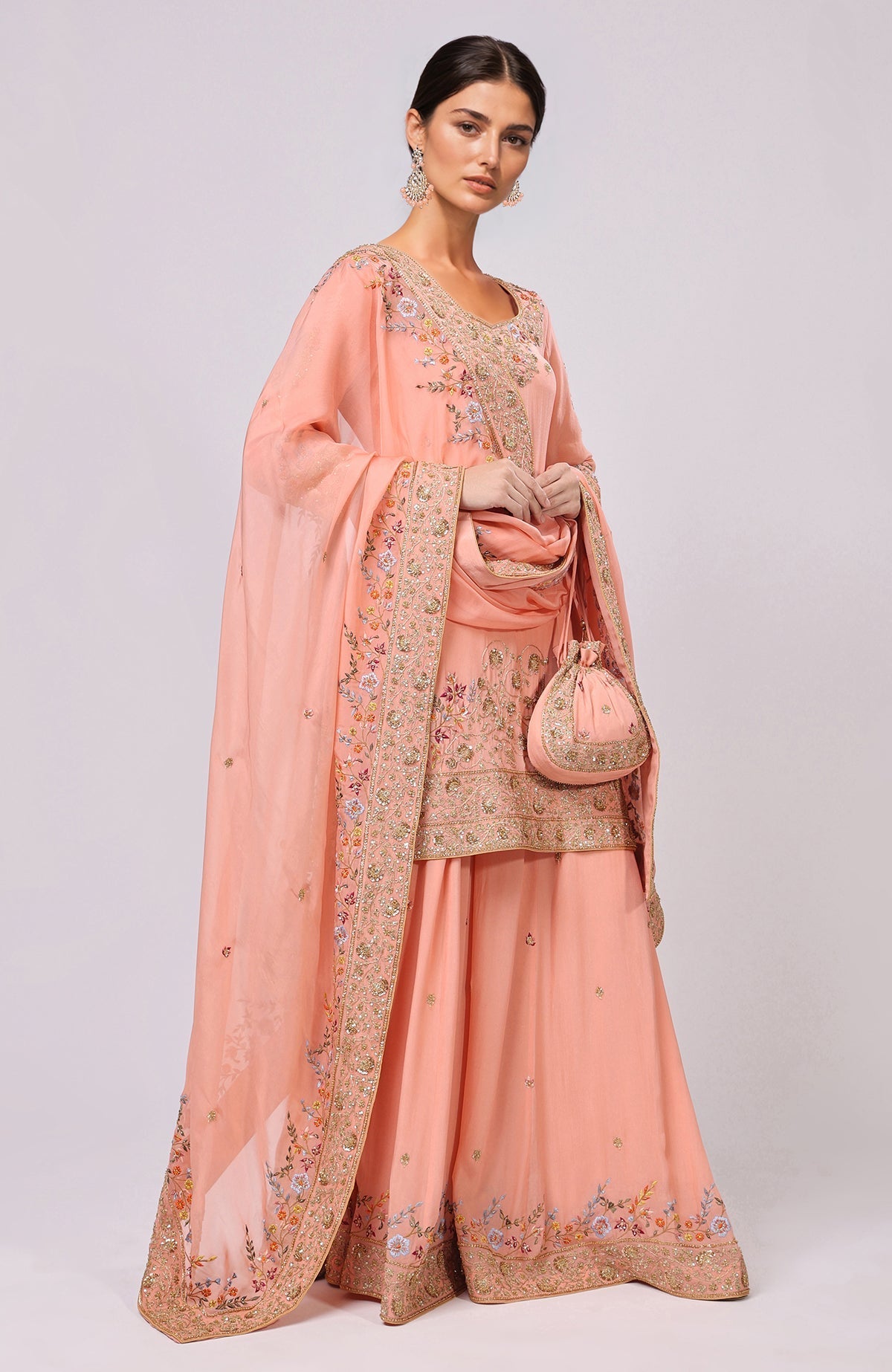 A woman models a salmon marori and resham hand-embroidered sharara set with a matching potli bag.