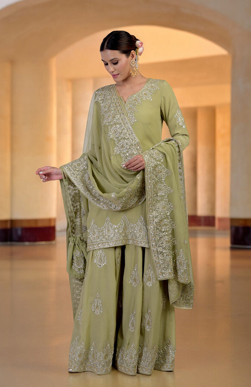 A woman models a bog green sharara set with gold Kashmiri tilla and zardozi embroidery.