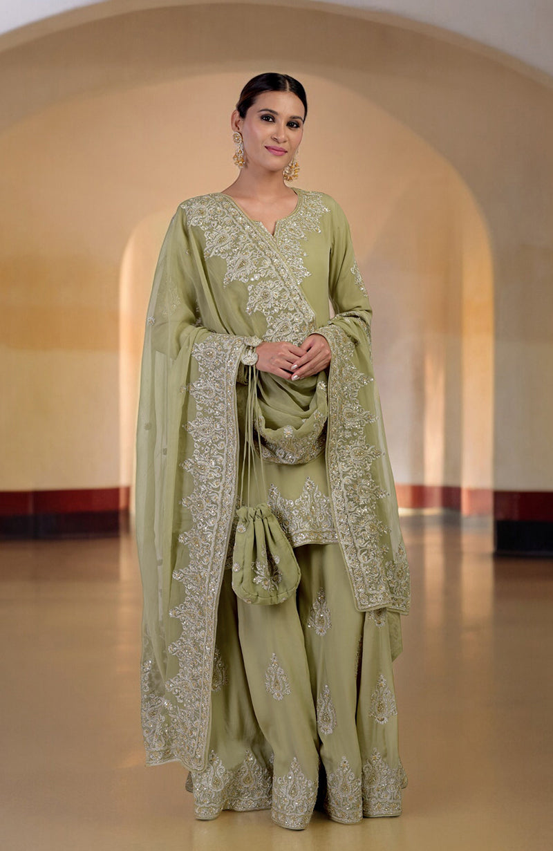 A woman in a bog green sharara set with gold embroidery and a matching potli bag.