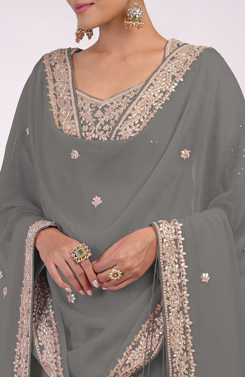 A woman models a grey sharara set with rose gold embroidery and two rings.