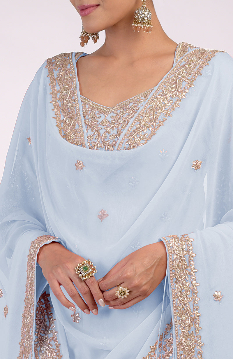 A woman models an illusion blue sharara set with intricate gold embroidery.