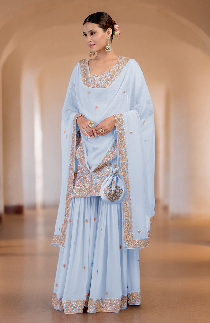 A woman models an illusion blue sharara set with intricate embroidery and a matching potli bag.