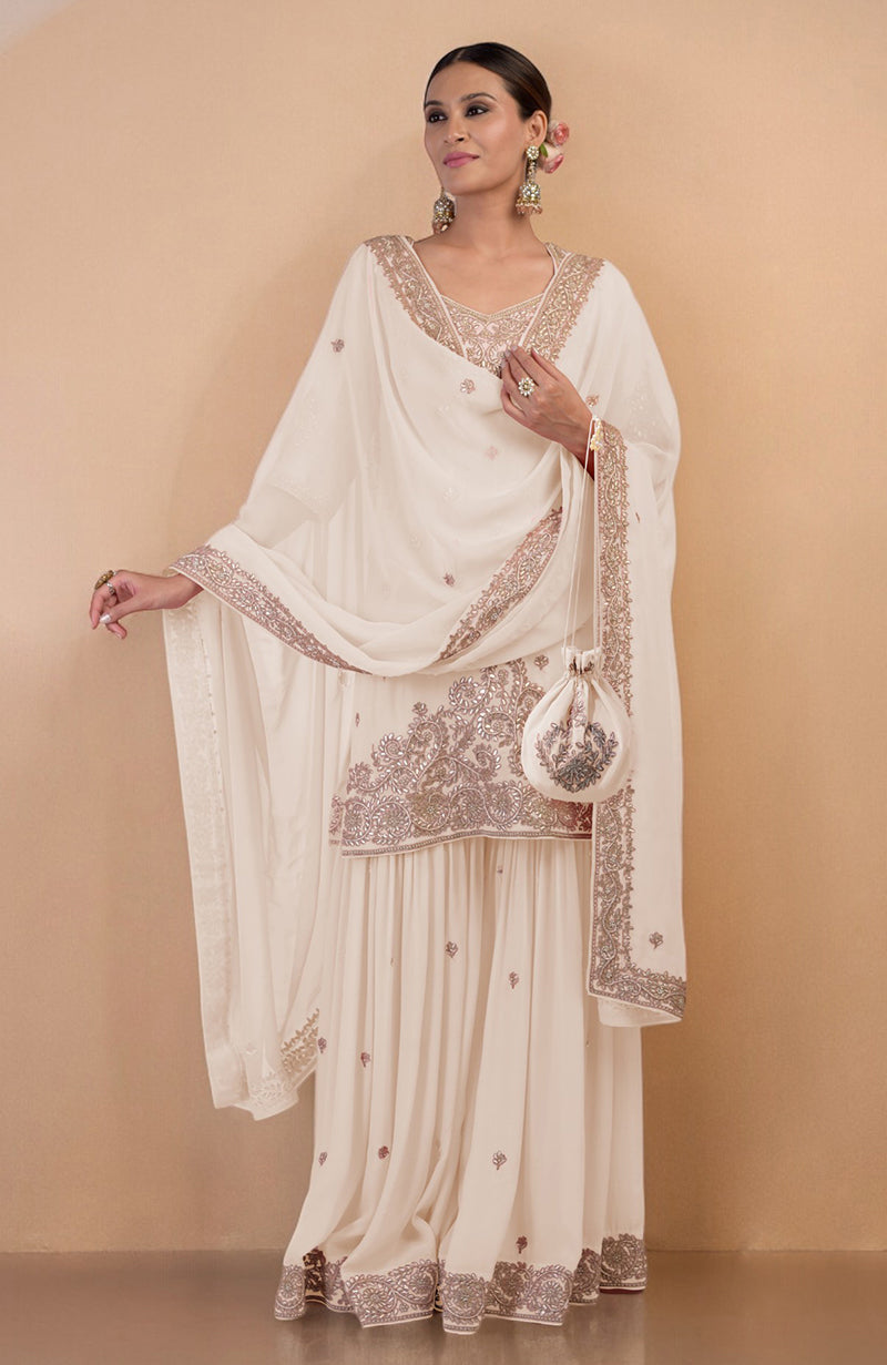 A woman models an off-white sharara set with intricate embroidery and a matching potli bag.