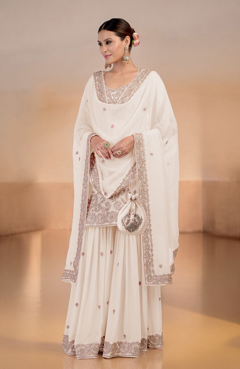 A woman models a white sharara set with intricate embroidery and a matching potli bag.