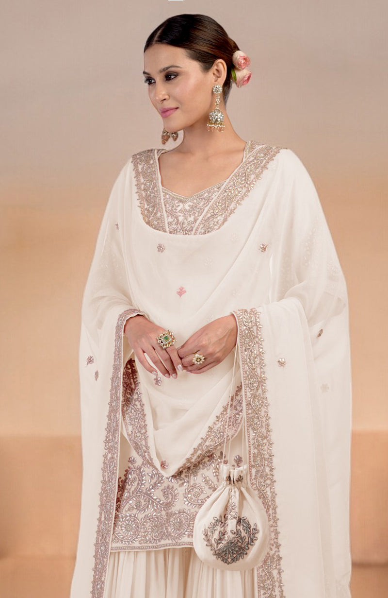 Woman in a sea salt sharara set with intricate embroidery and a matching potli bag.