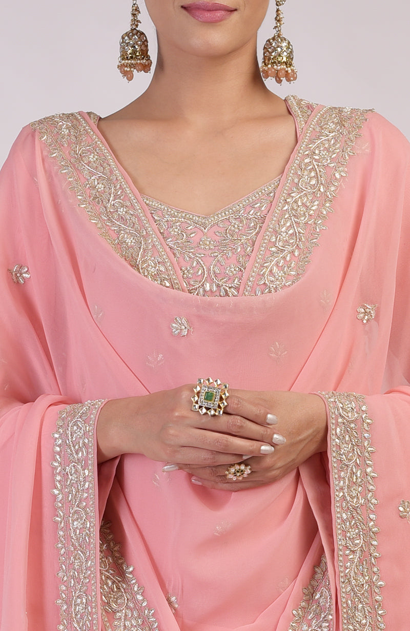 A woman models a peony pink sharara set with intricate gold embroidery and jewelry.