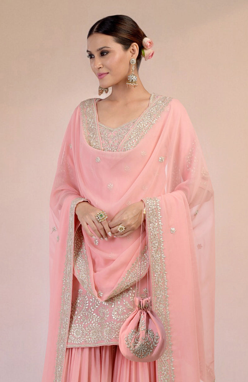 A woman models a peony pink sharara set with intricate silver embroidery and a matching potli bag.