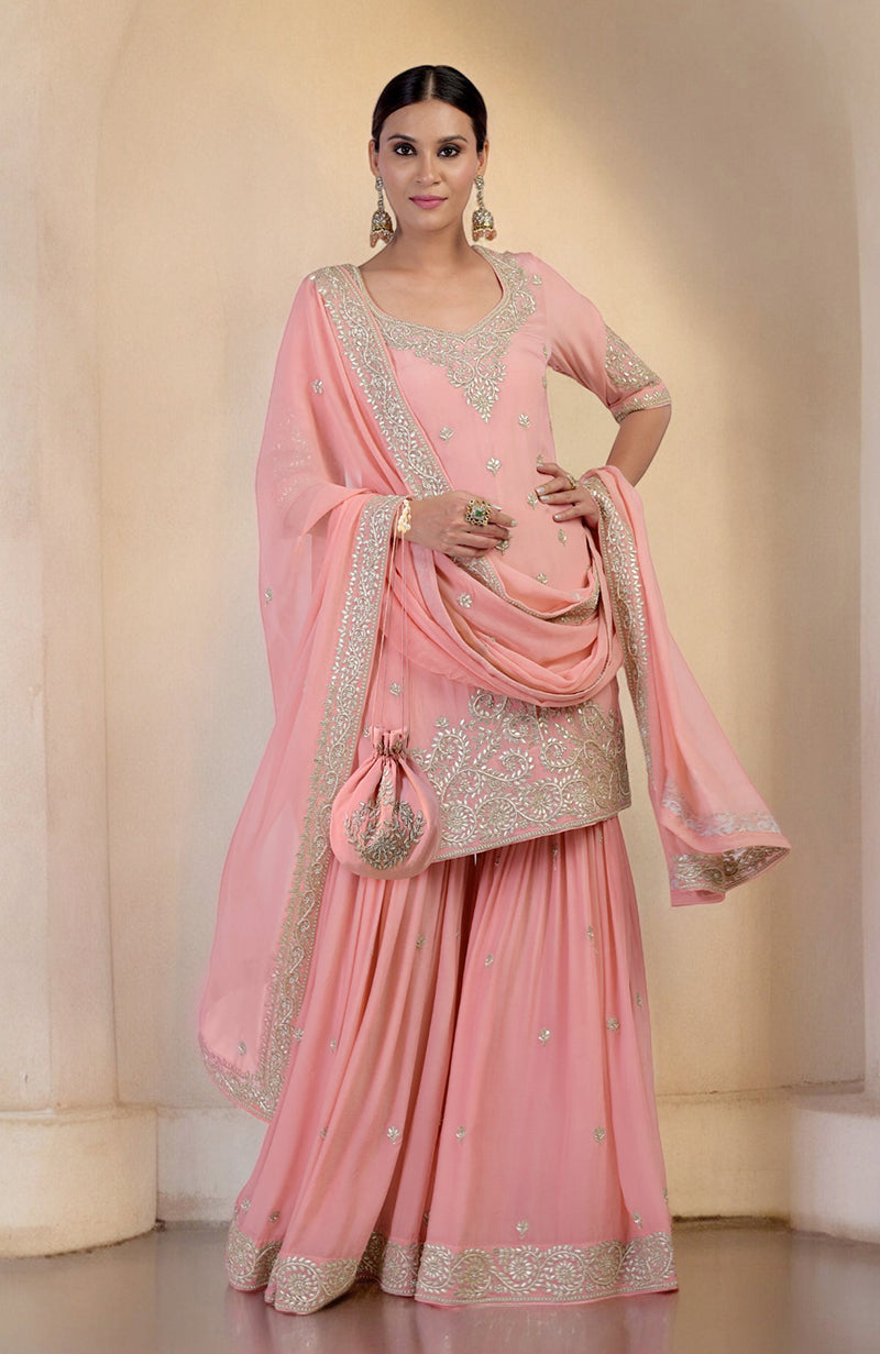 A woman models a peony pink sharara set with silver embroidery and a matching potli bag.
