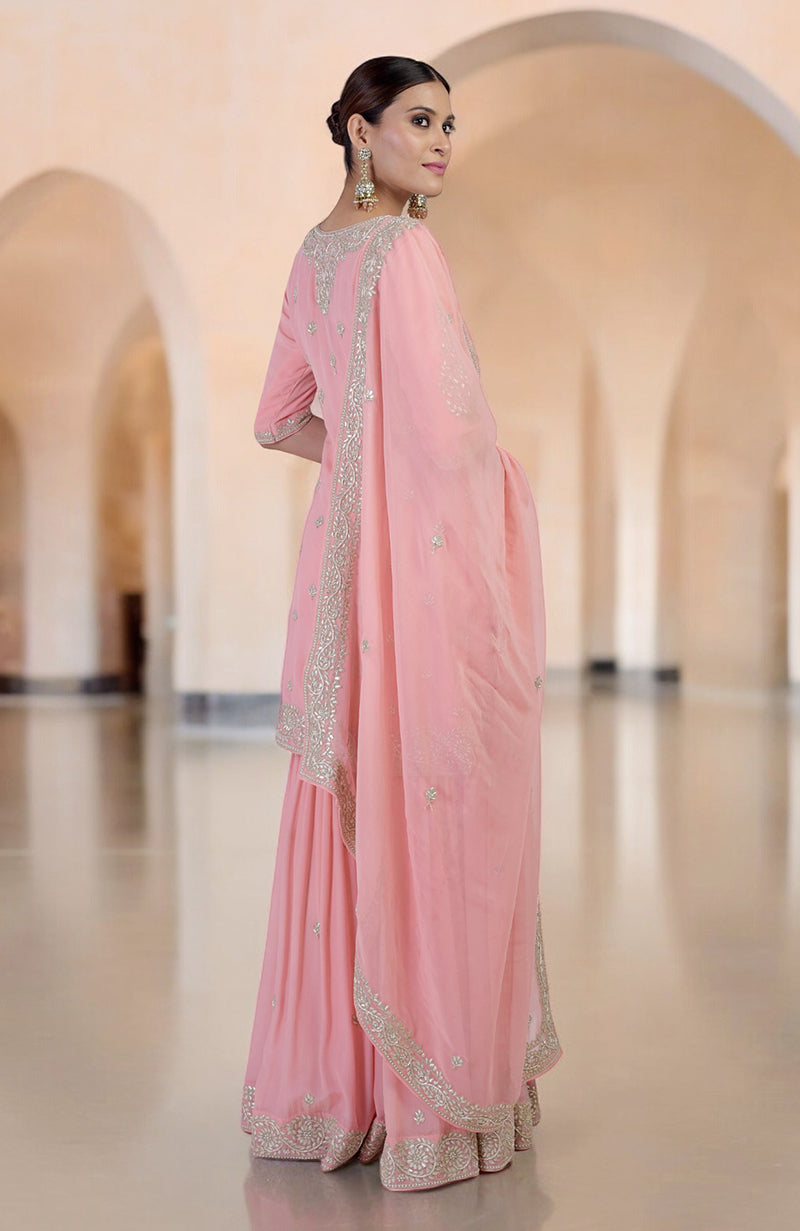 A woman in a pink sharara set with silver embroidery looks over her shoulder.
