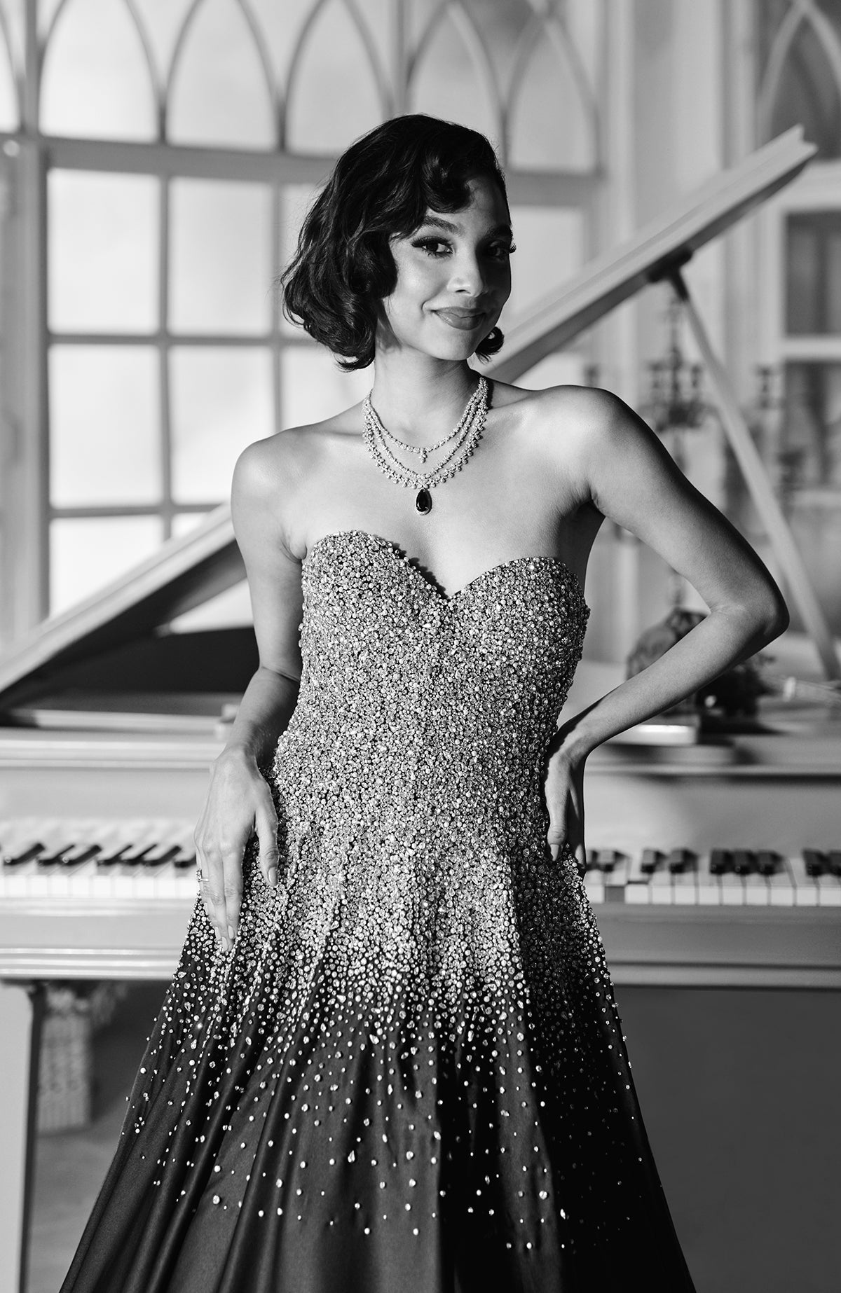 A woman in a black crystal hand-embroidered ball gown stands by a piano.