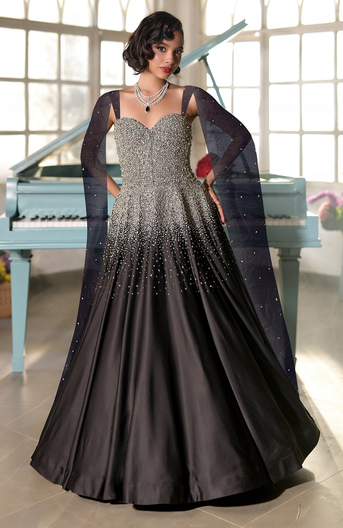 A woman models a black princess gown with a crystal-embroidered bodice and sheer sleeves.