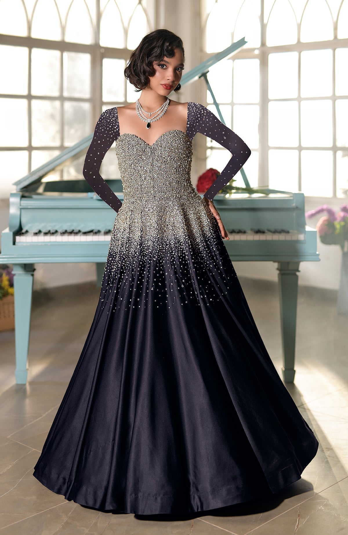 A woman in a black and gold crystal-embroidered princess gown stands by a piano.