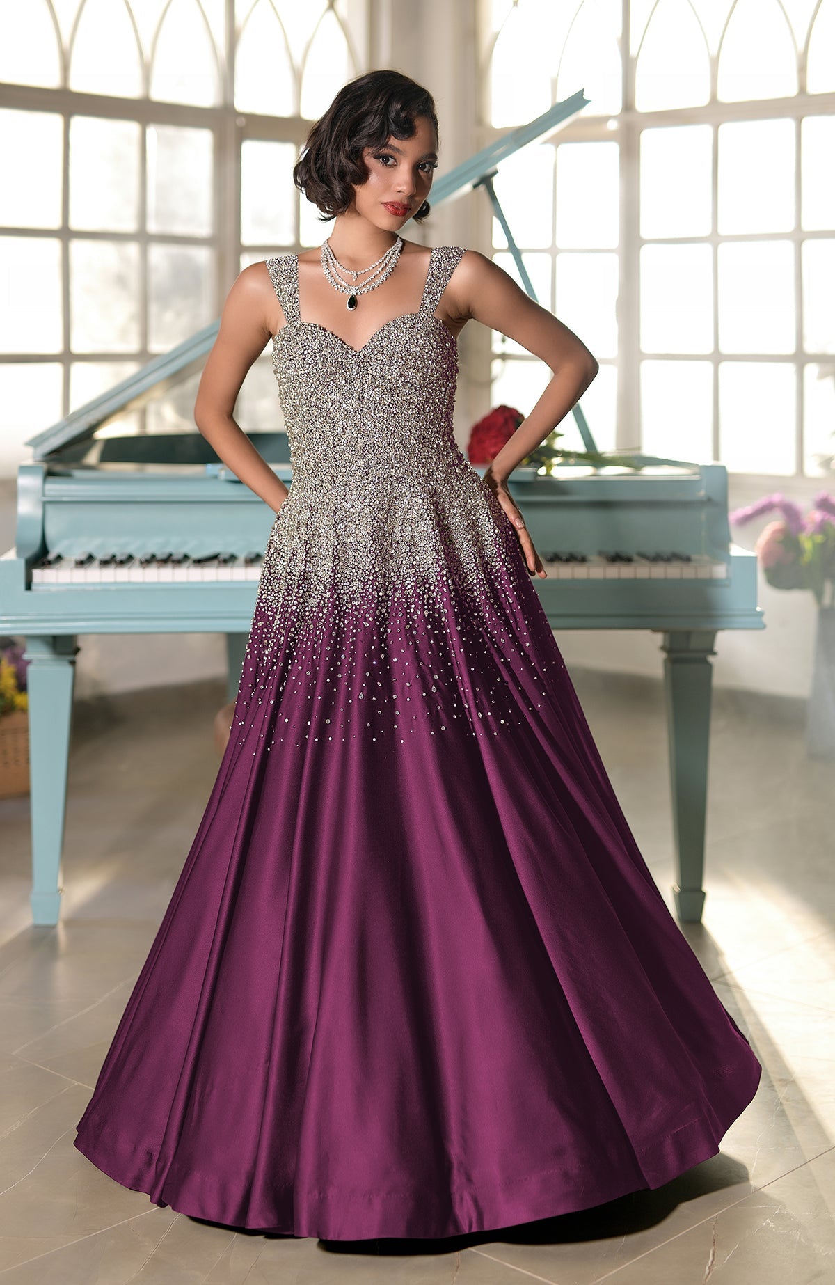 A woman in a crystal-embroidered princess gown with a purple skirt stands by a piano.