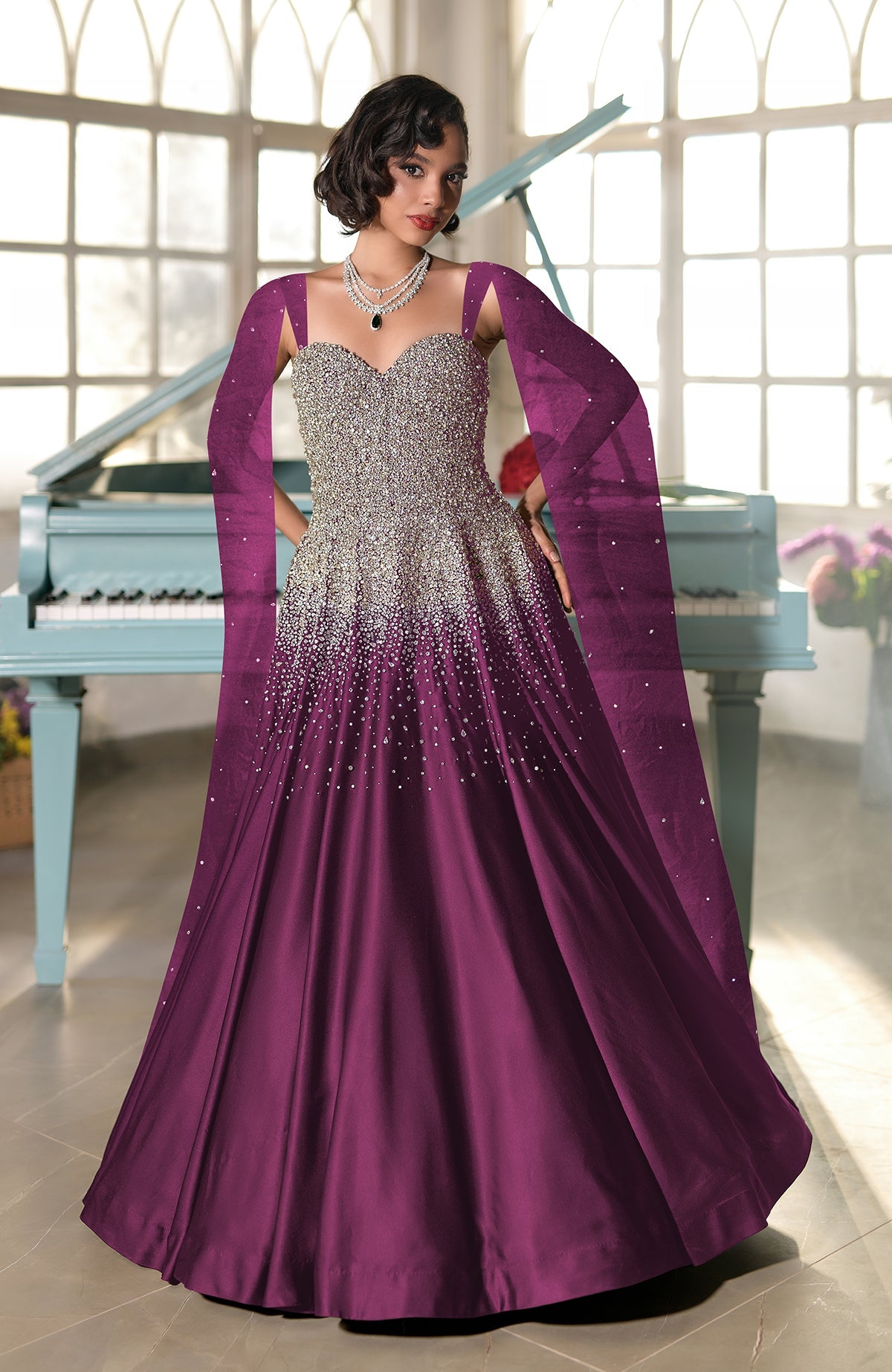 A woman in a purple crystal-embroidered princess gown with a flowing cape stands by a piano.