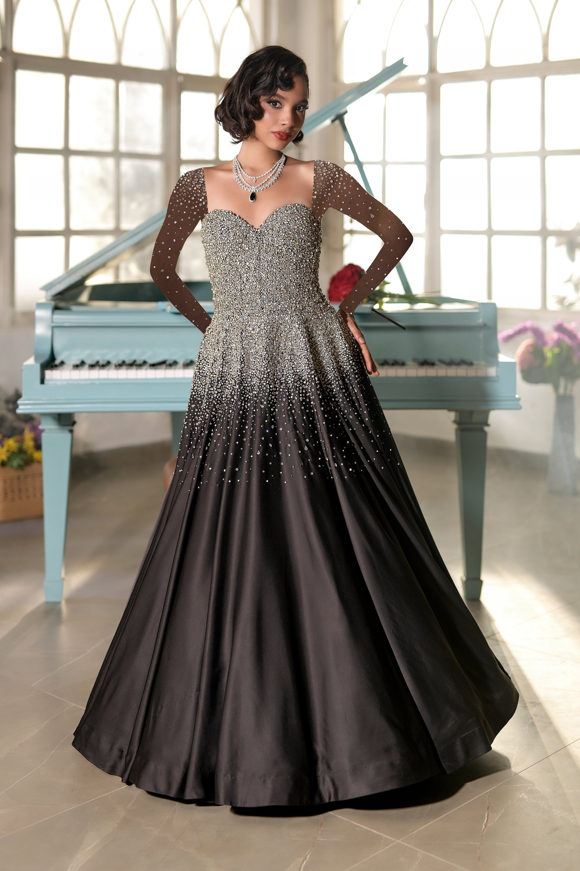 A woman in a black and silver crystal-embroidered princess gown stands by a light blue piano.