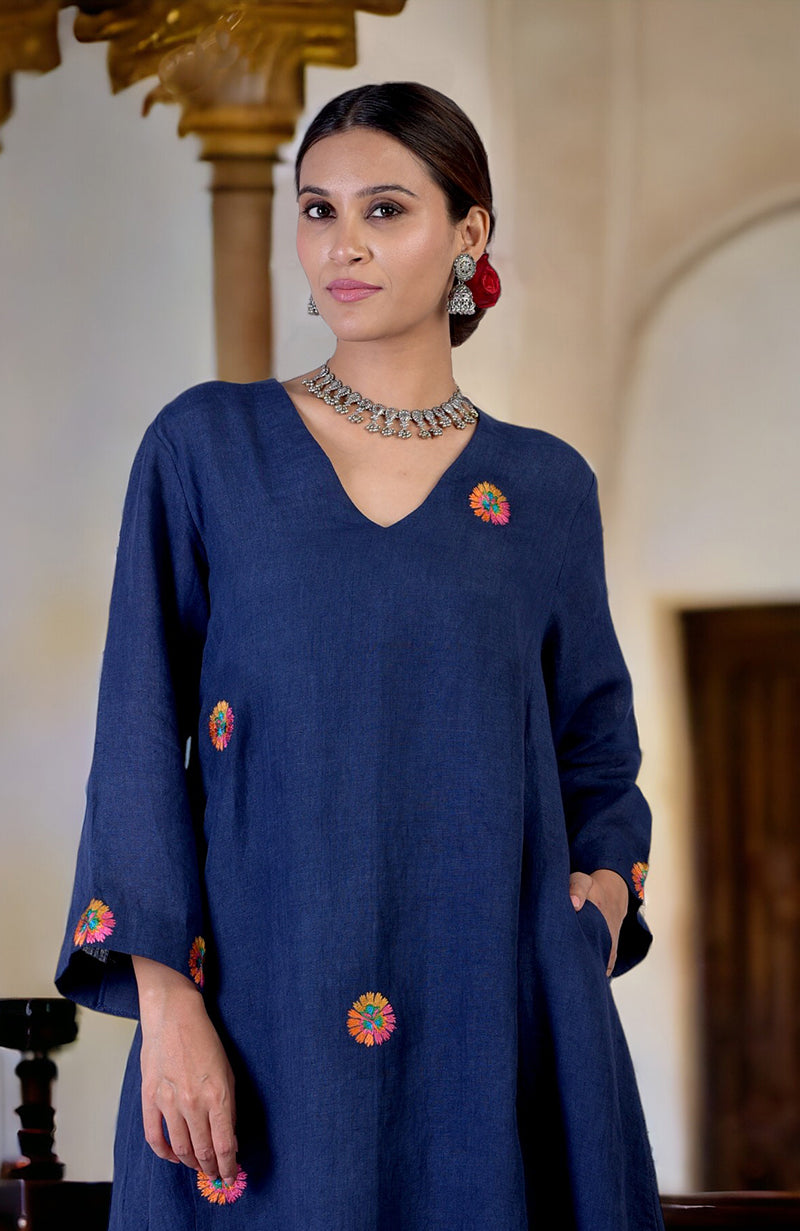A woman models a navy blue linen kurta with colorful floral embroidery and pockets.