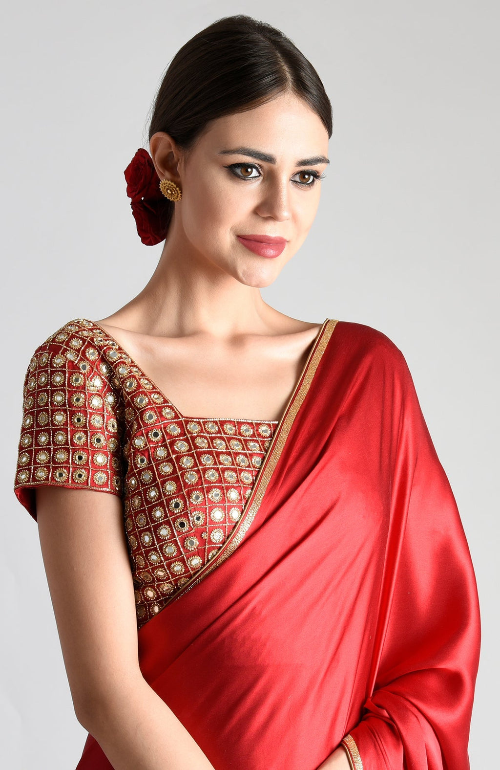 A woman models a red mirror work and zardozi hand embroidered blouse with a red saree.