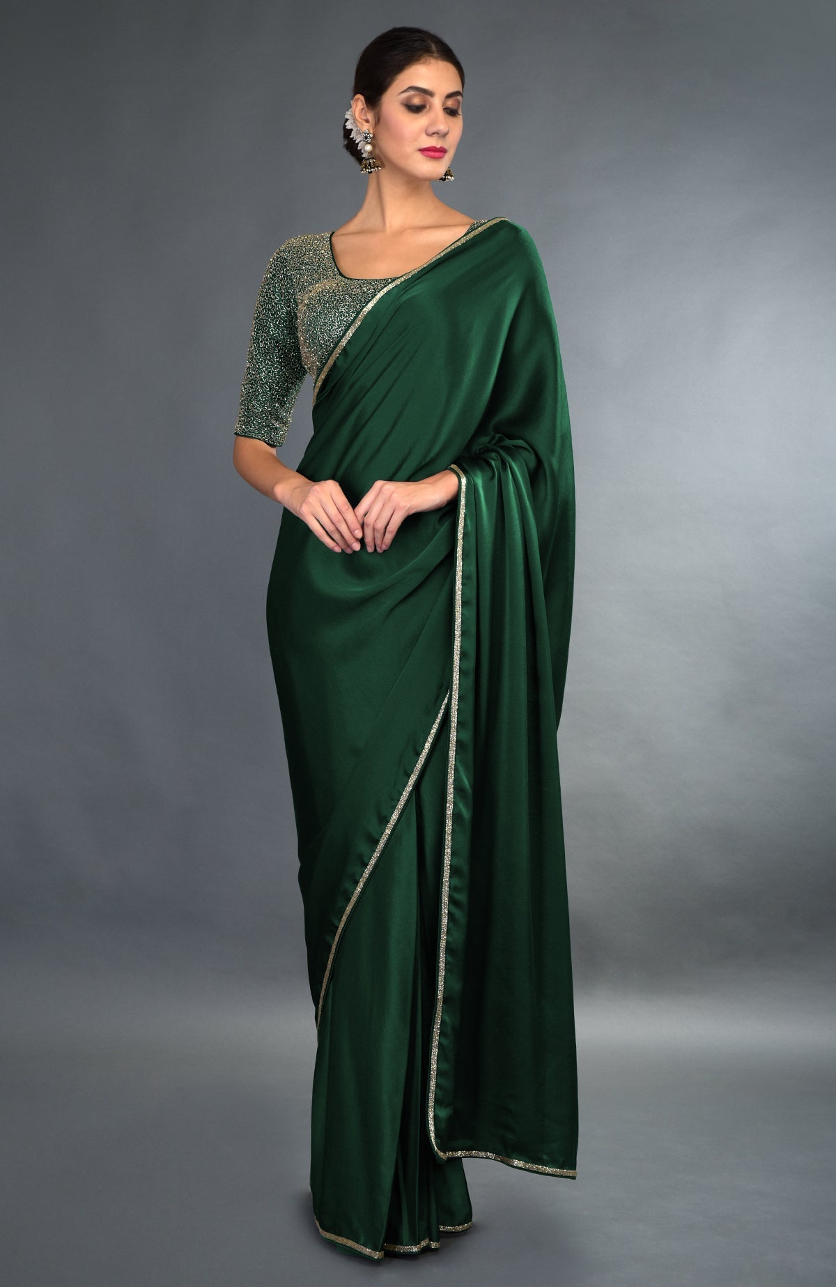 An emerald green satin saree with gold zardozi borders and a matching embroidered blouse.