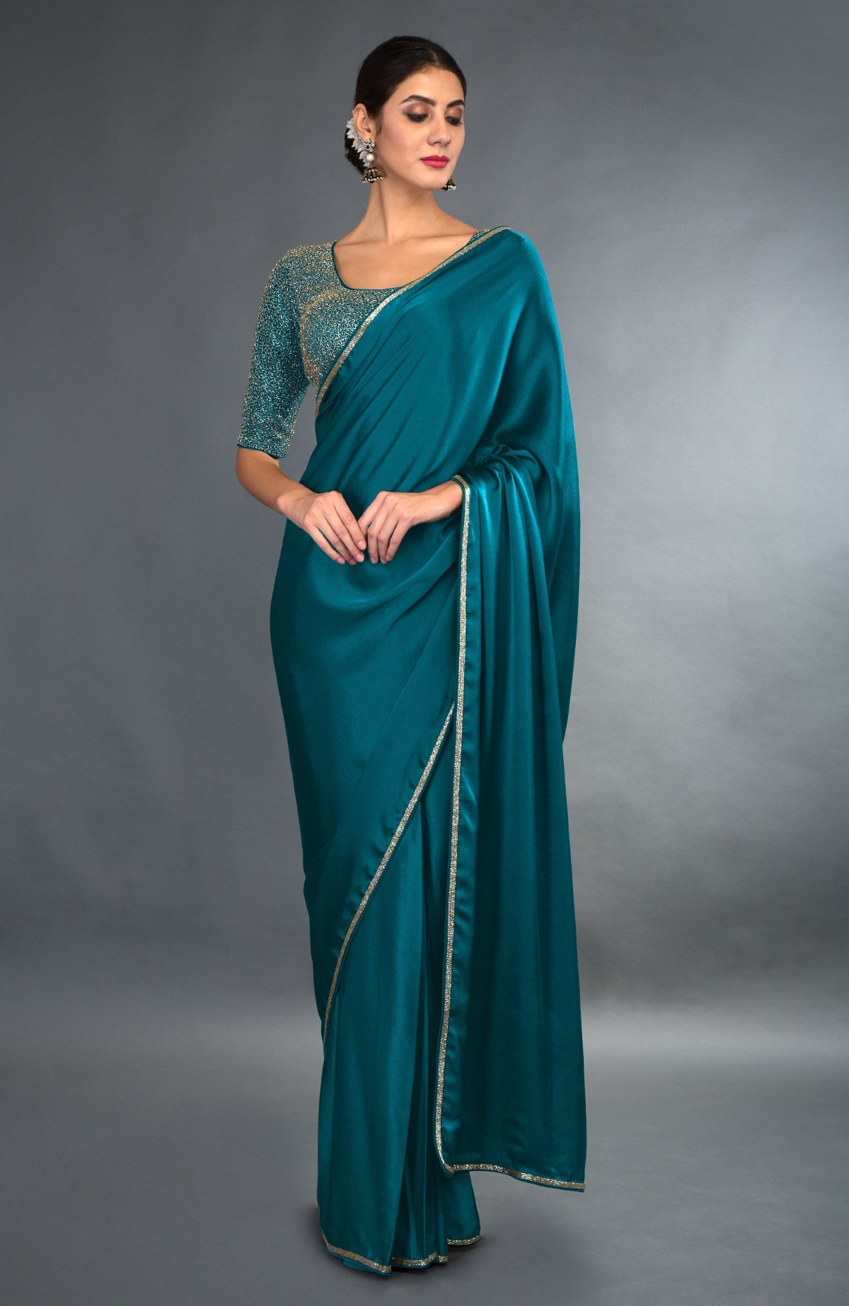 A woman models a peacock blue satin saree with gold zardozi embroidery.