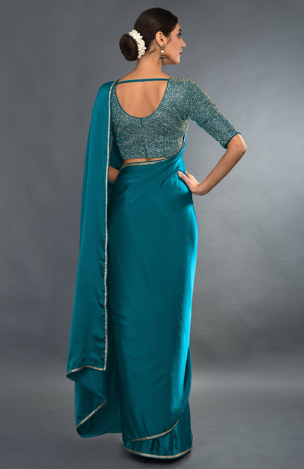 Peacock blue satin saree with a zardozi embroidered blouse, worn by a model.