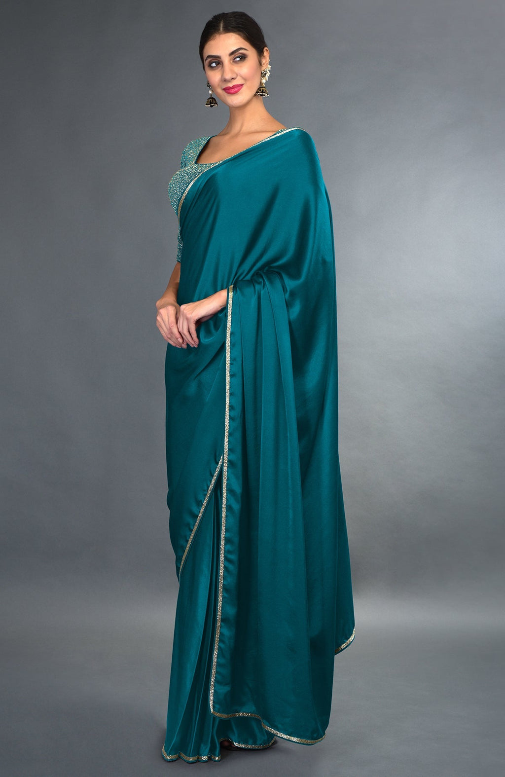 A woman models a peacock blue satin saree with gold zardozi borders and a matching blouse.
