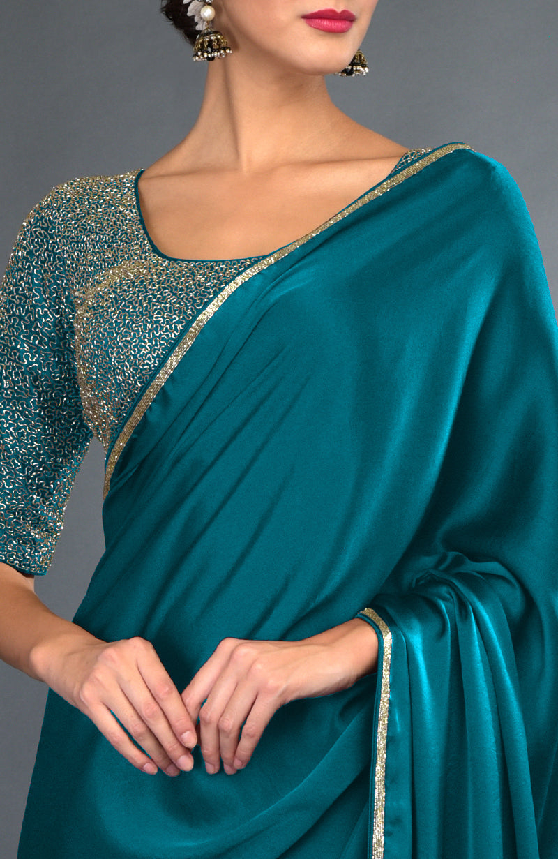 Peacock blue satin saree with gold zardozi embroidery on the blouse and borders.