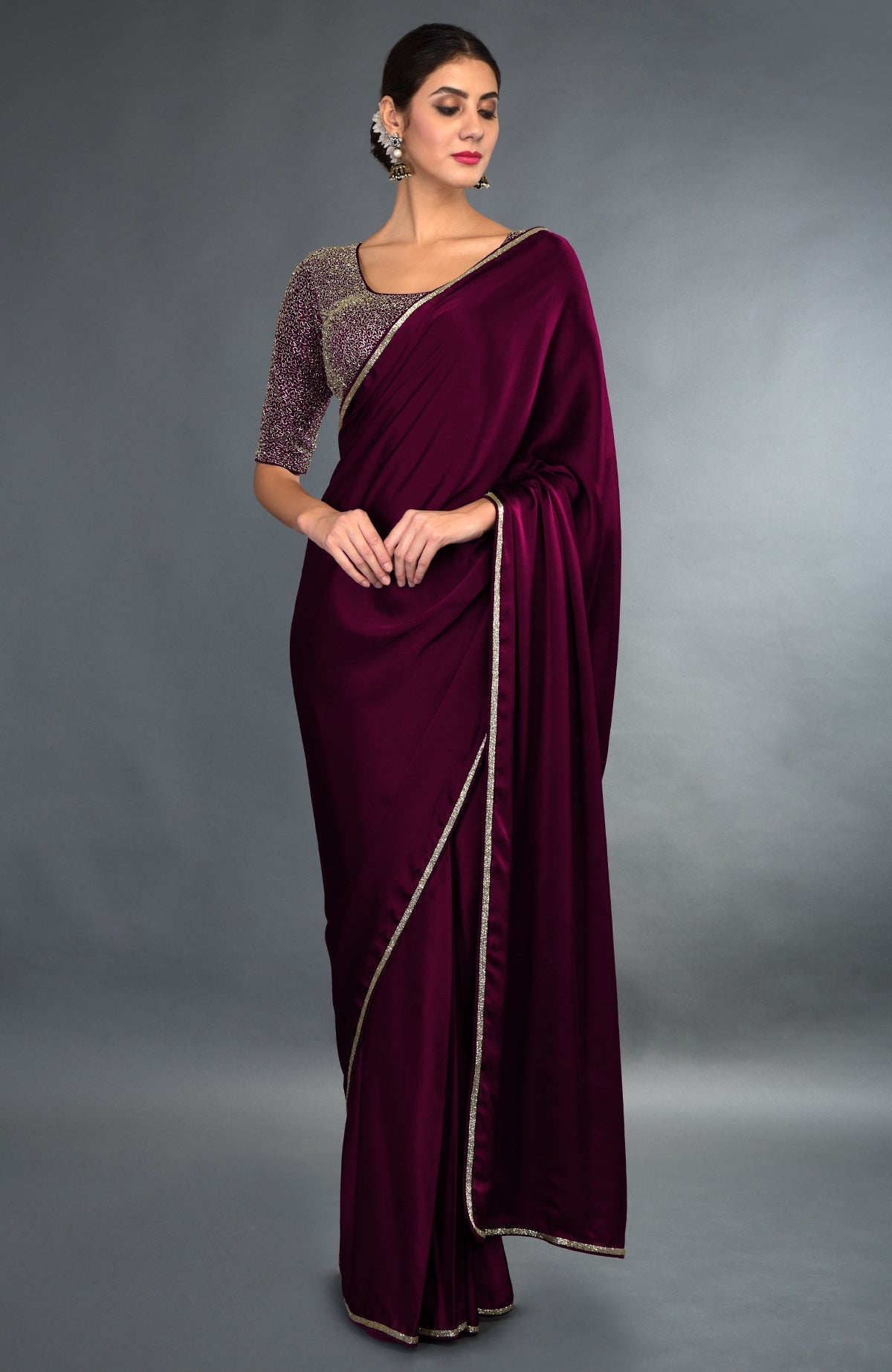 A woman models an emerald green satin saree with zardozi borders and an embroidered blouse.