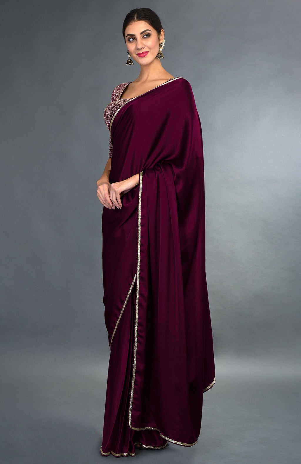 A woman models a burgundy satin silk saree with zardozi borders and an embroidered blouse.