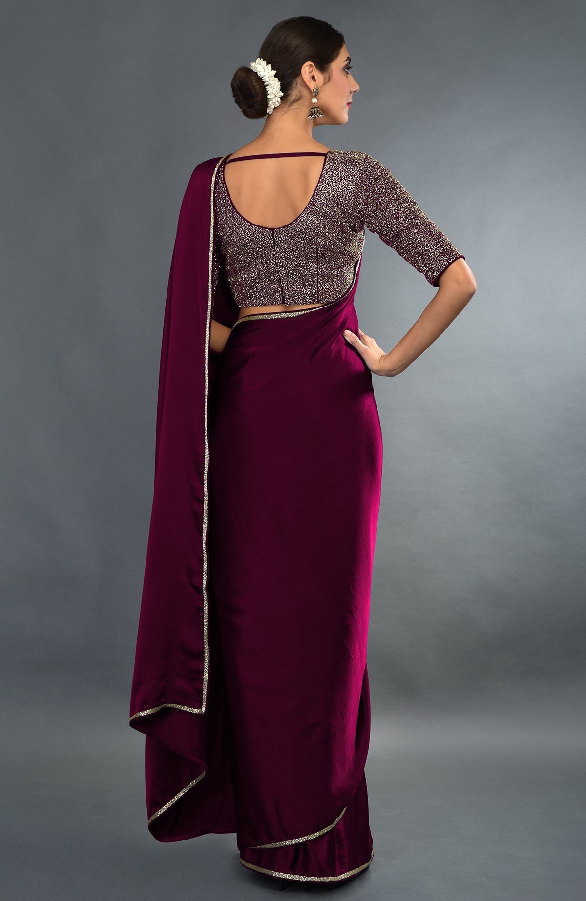 A woman models a burgundy zardozi hand-embroidered saree and blouse from behind.