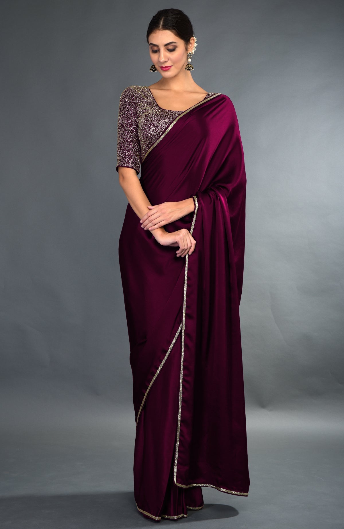 A woman models a burgundy satin silk saree with gold zardozi borders and an embroidered blouse.