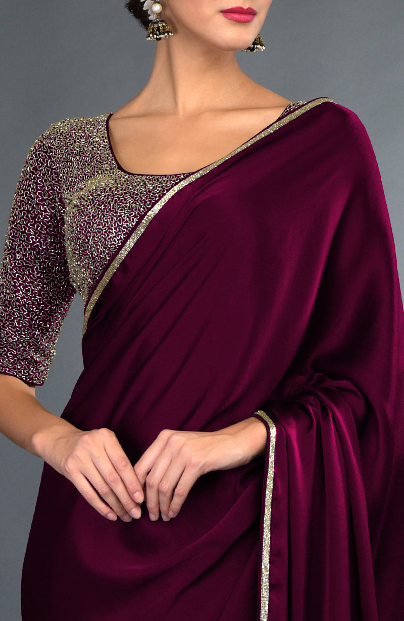 A woman models a burgundy satin silk saree with gold zardozi embroidery.