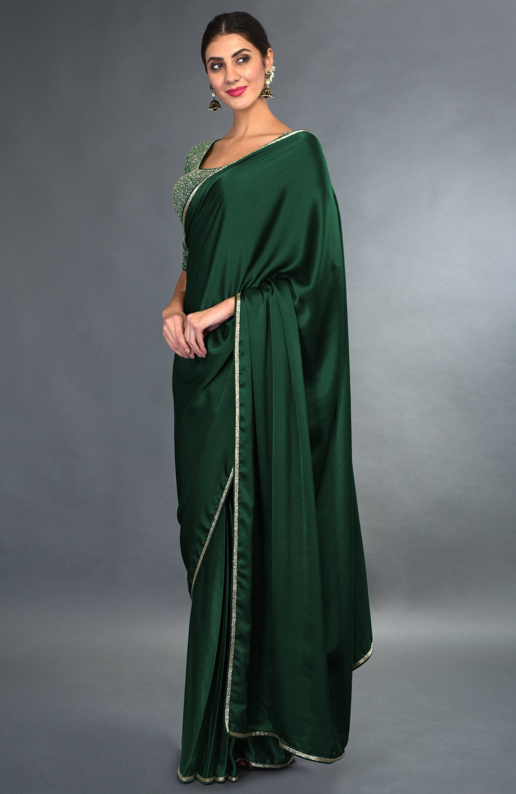 An elegant woman models an emerald green satin saree with gold zardozi borders.