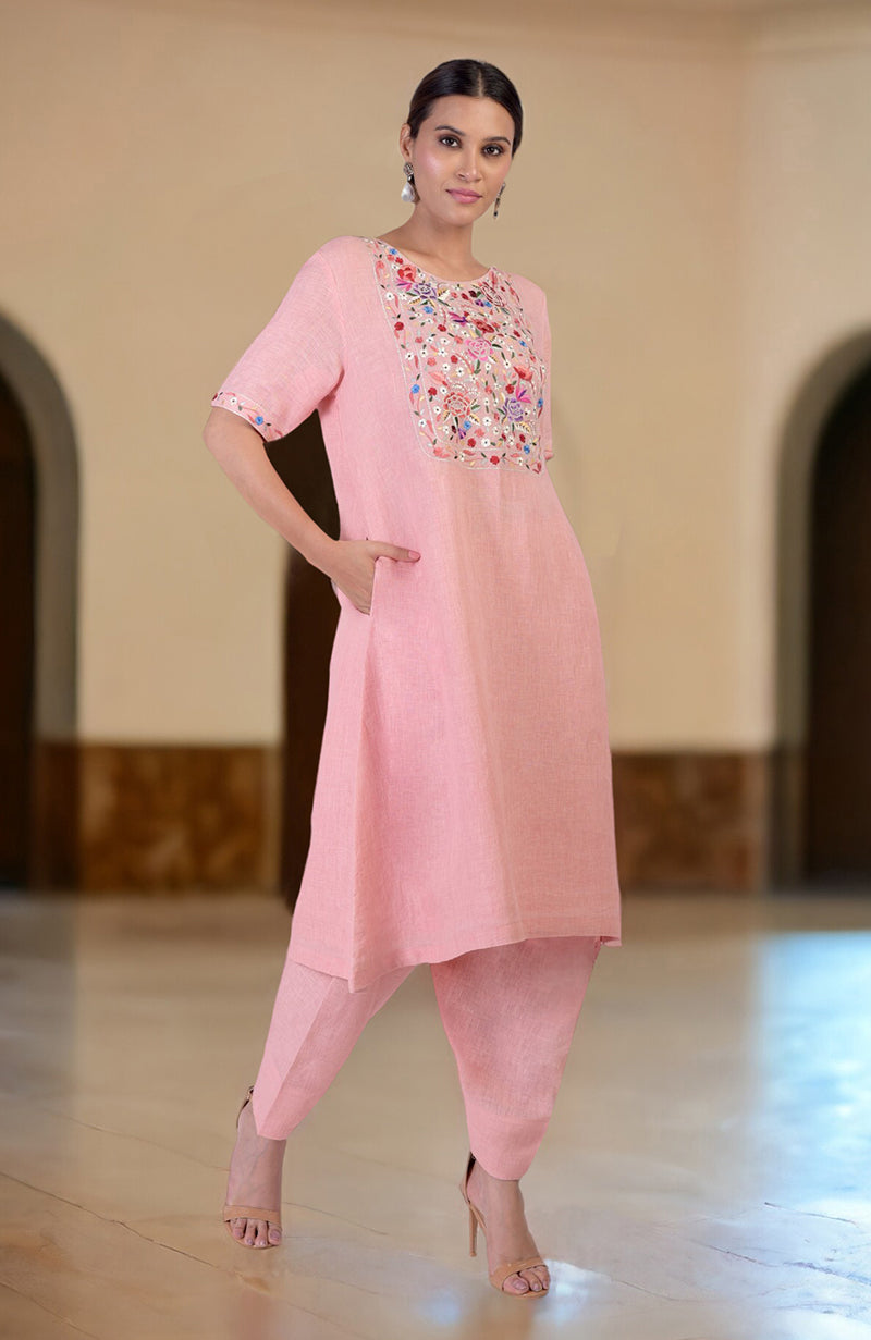 A woman models a pink linen kurta set with Parsi Gara embroidery.
