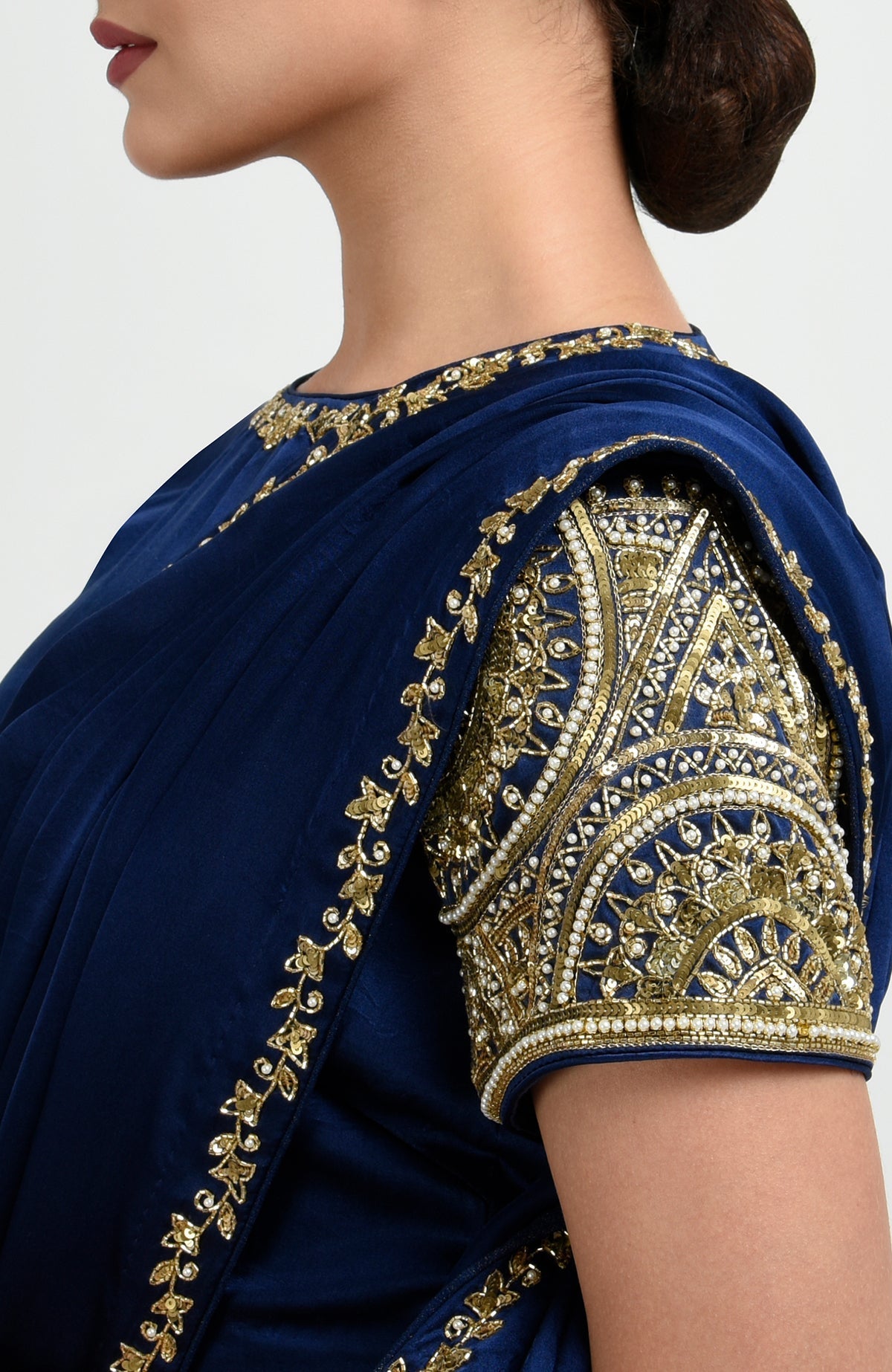 A woman models a sapphire blue saree with gold zardozi and pearl bead embroidery.