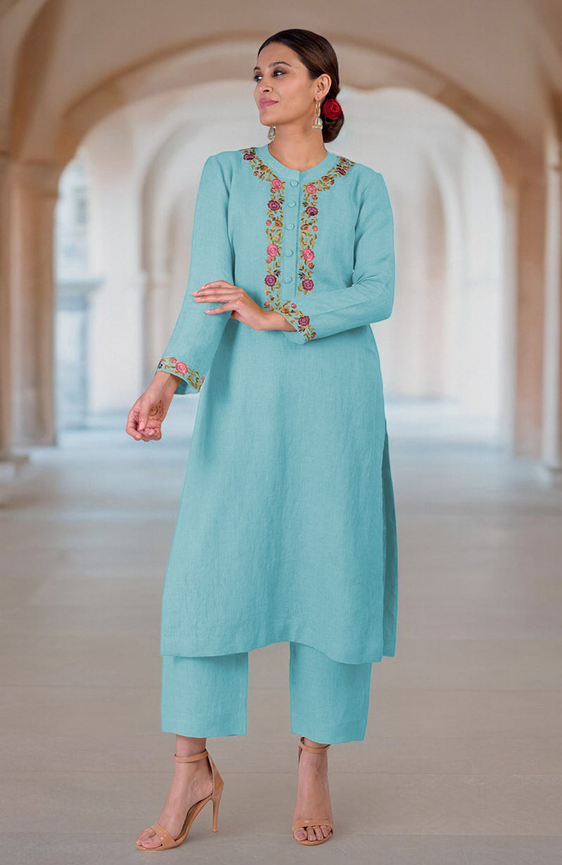 A woman models a light blue linen kurta set with colorful floral embroidery.