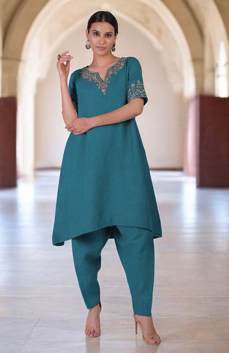 A woman models a teal linen kurta set with gold embroidery and a high-low hem.