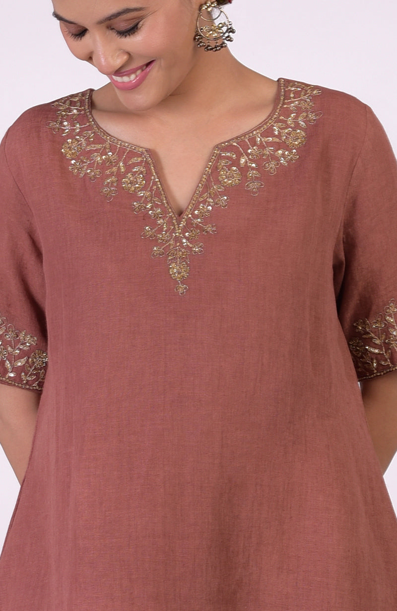 A woman models a chutney-colored linen kurta with gold marori embroidery on the neckline and sleeves.