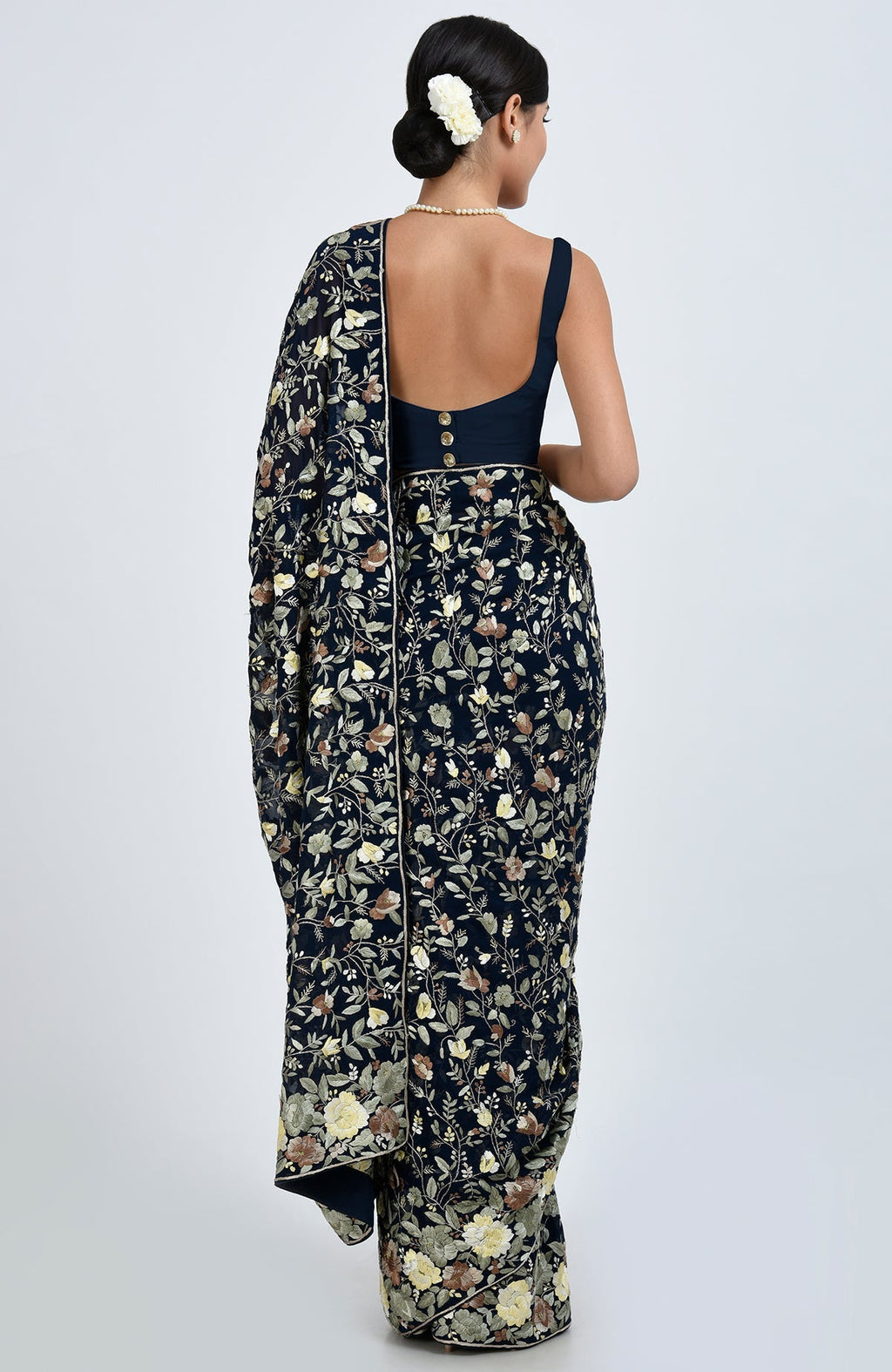 A woman from behind wears a midnight blue Parsi Gara hand-embroidered saree with floral patterns.