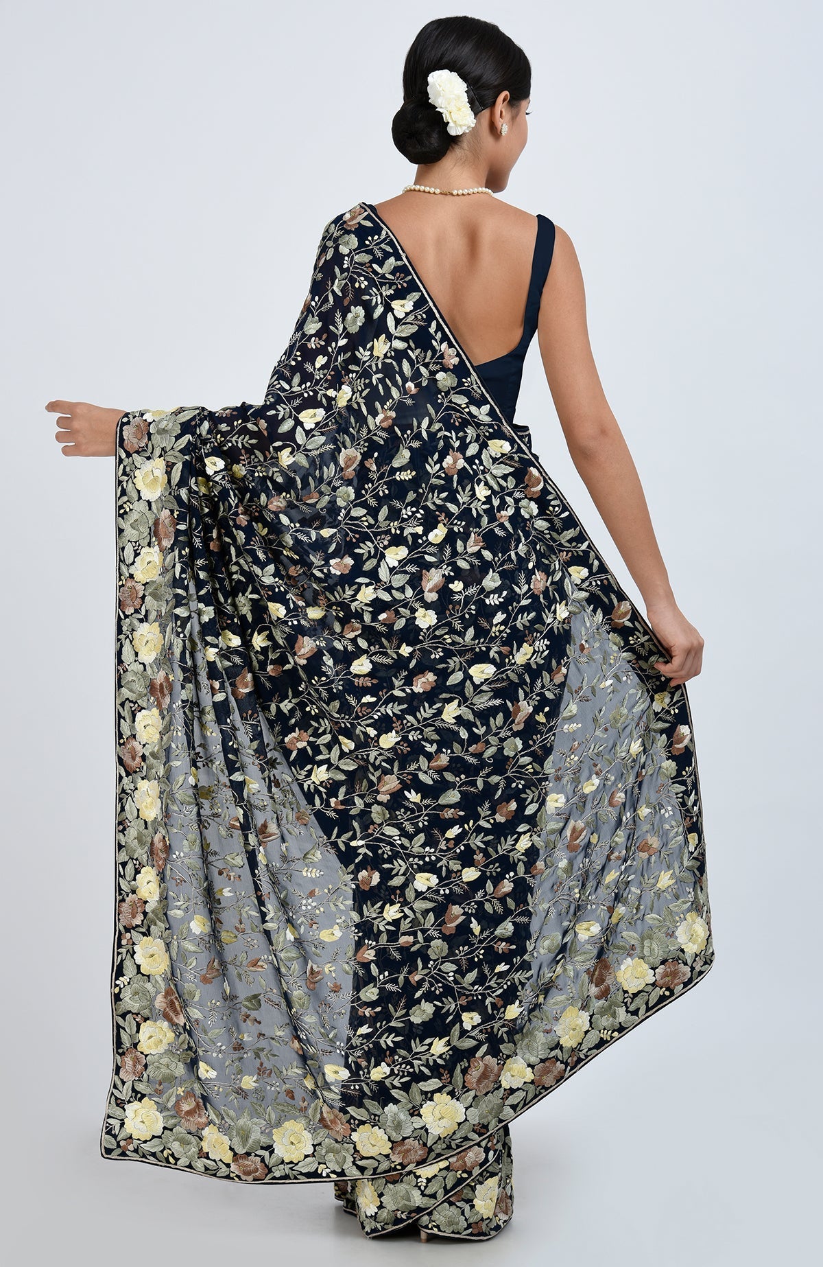 A woman from behind models a midnight blue Parsi Gara hand-embroidered saree with floral patterns.