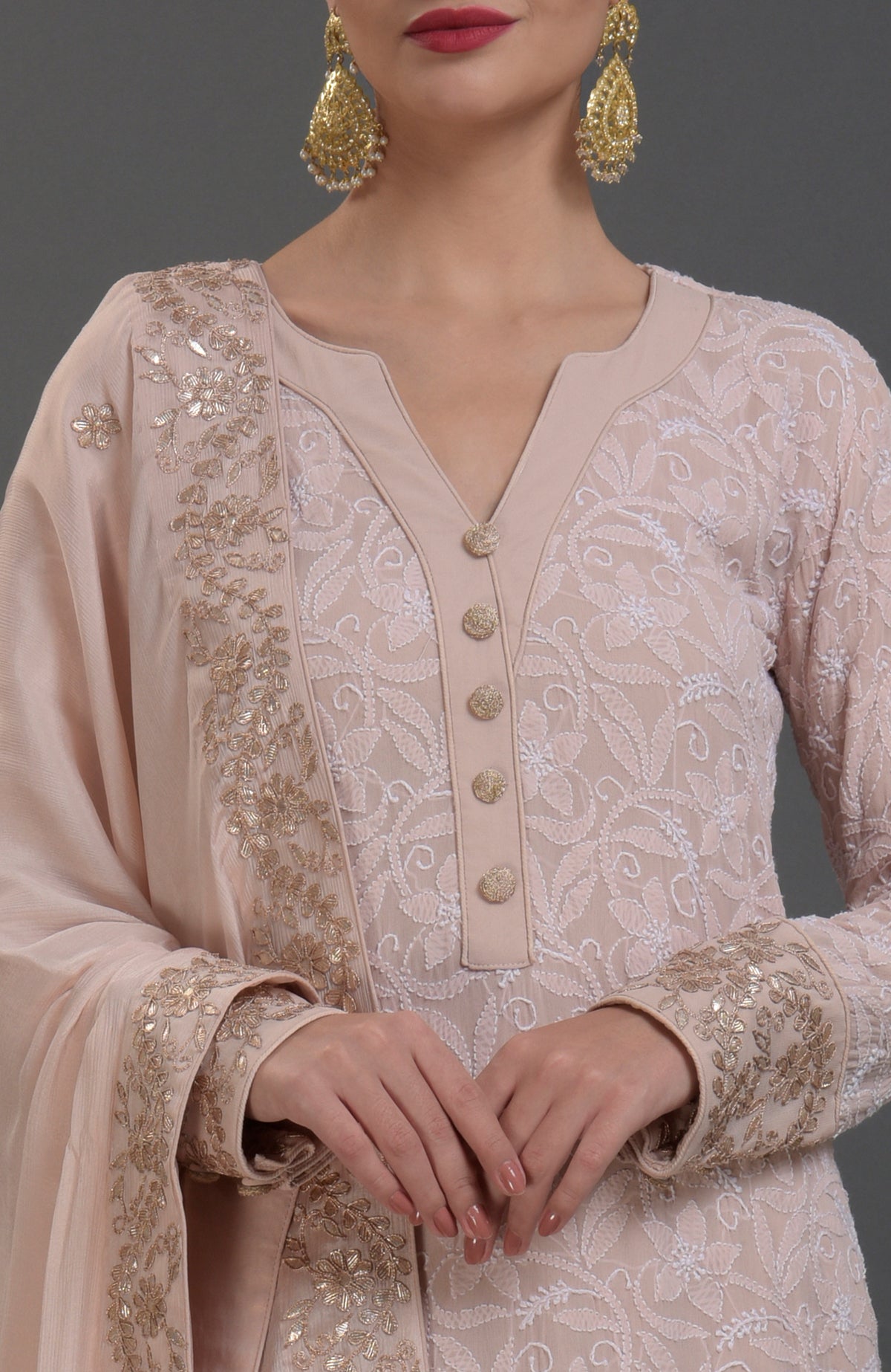A woman models an oyster pink chikankari and gota patti hand-embroidered sharara suit.