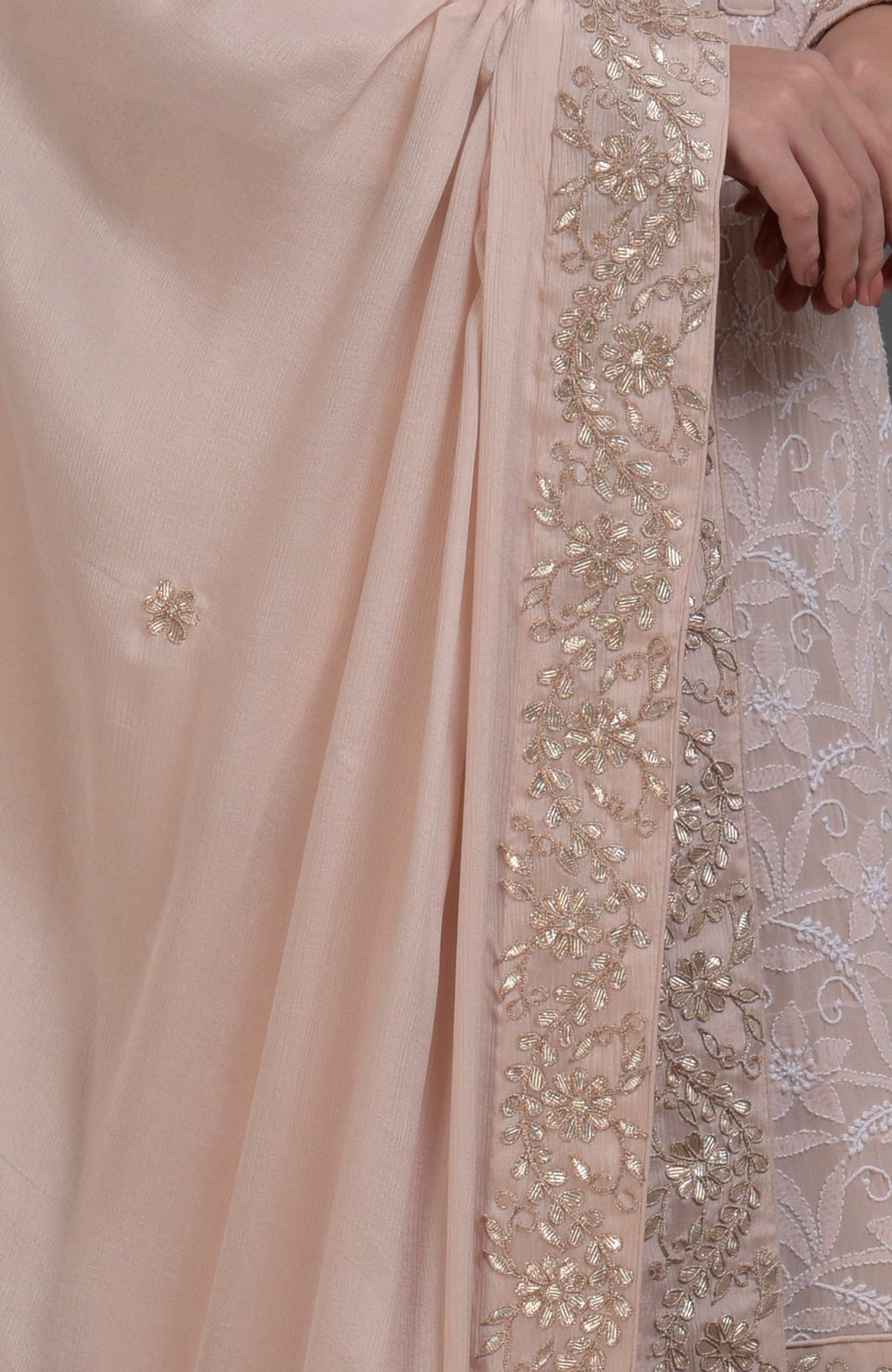 Close-up of an oyster pink fabric with gold embroidery and a hand.