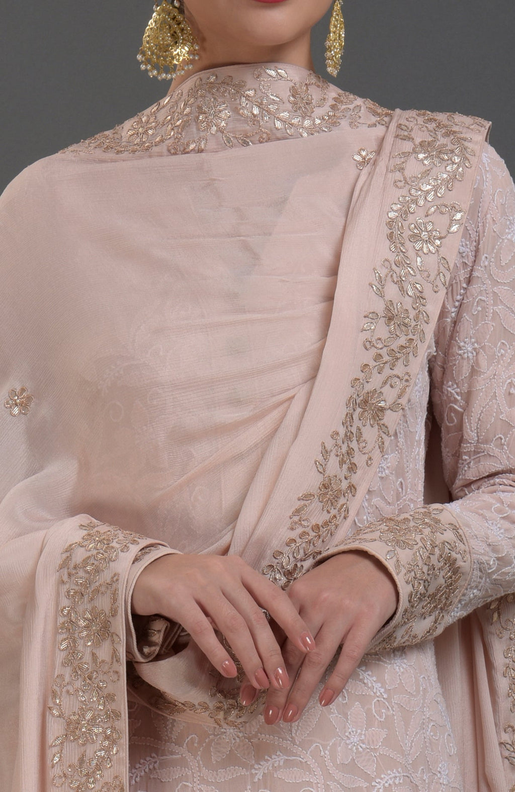 A woman models an oyster pink Chikankari and Gota Patti hand-embroidered sharara suit.